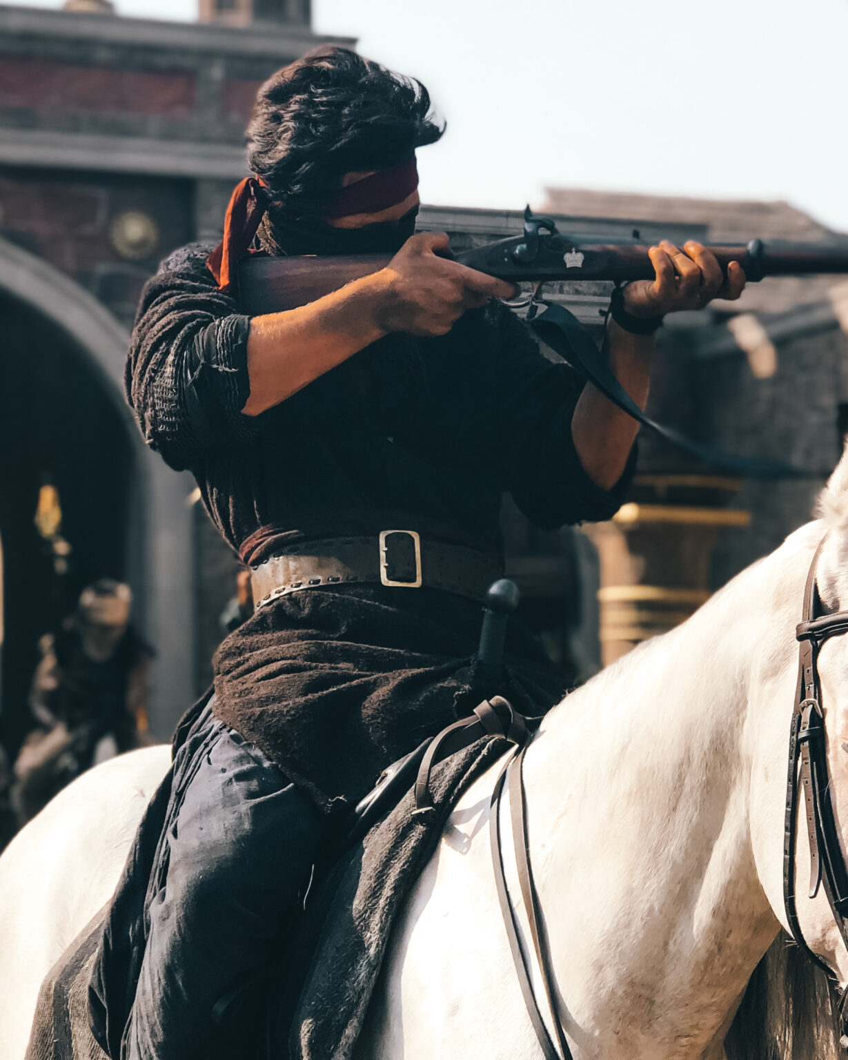 Skilled stunt double holding a gun on a white horse on a movie set in India