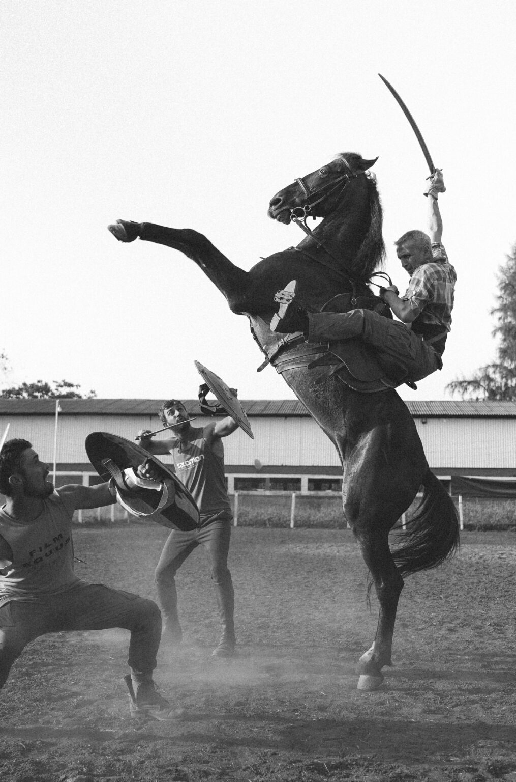 Horse rearing with skilled stuntmen holding swords and shields, practicing for a movie scene.